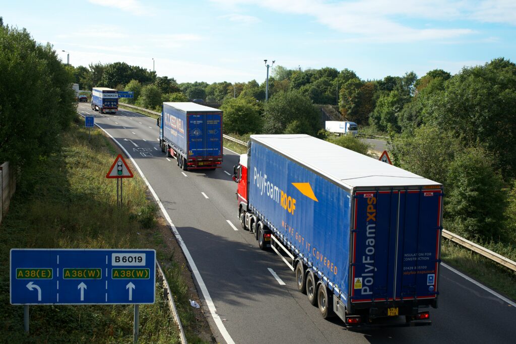 Cargo trucks on A38 highway, Mansfield, UK, surrounded by summer greenery and clear skies.
